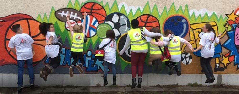 Foto: Kinder von hinten springen vor eine Bunt bemalten Wand
