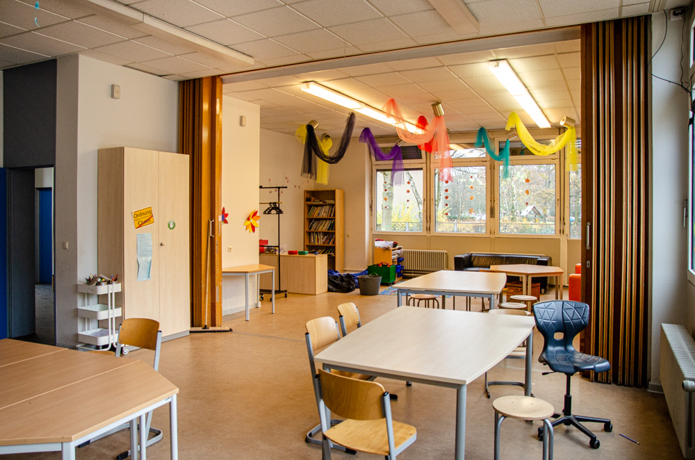 Foto: Raum mit gruppierten Tischen und Stühlen, Spielzeug und bunten Girlanden an der Decke