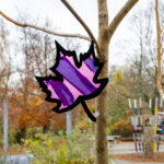 Foto: gebasteltes buntes Ahornblatt klebt an einer Fensterscheibe