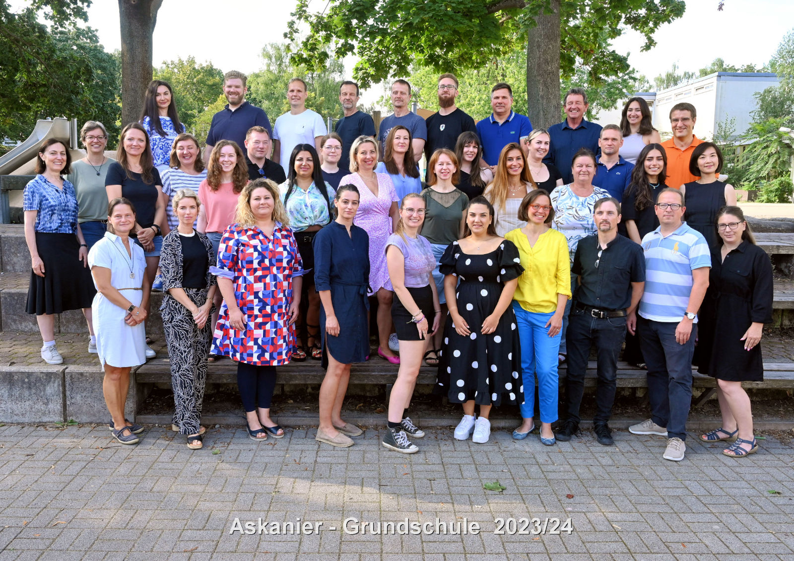 Personal Askanier-GS 2023-2024 Foto: Gruppe von Männern und Frauen in Gruppenfotopose auf eine Tribüne mit Blick zum Betrachter. Vorderste Reihe sitzt.